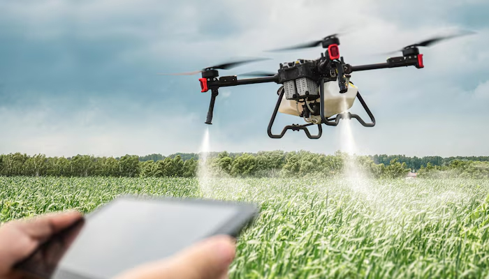 A quadcopter drone spraying crops over a green agricultural field, controlled remotely by a person holding a tablet device, showcasing modern precision farming technology.